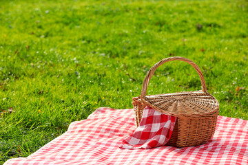 One picnic wicker basket with checkered napkin and blanket on green grass. Space for text