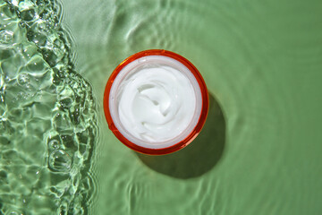 Jar with cream in water on light green background, top view. Cosmetic product