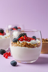 Tasty yogurt with fresh berries and granola in glass on violet background