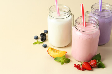Different tasty yogurts in mason jars, peach, fresh berries and mint on pale yellow background, space for text