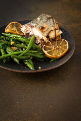 Savor the wholesome flavors of baked green beans with onions and baked mackerel, elegantly presented on a plate against a brown background, ideal for a nutritious and delicious meal