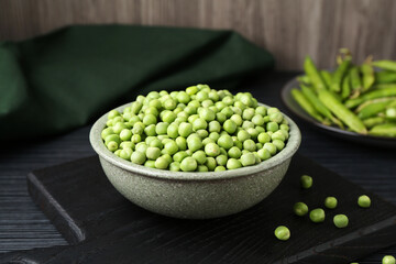 Fresh green peas in bowl on black wooden table, closeup