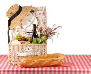 Picnic wicker basket with food, tableware, bottle of wine and flowers on table against white...