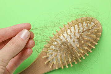 Woman taking her lost hair from brush on light green background, closeup. Alopecia problem