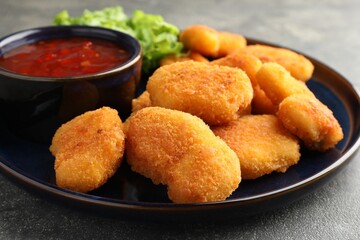 Tasty chicken nuggets with chili sauce on grey table, closeup