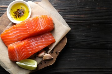Pieces of fresh salmon, garlic, lime, oil and spices on wooden table, top view. Space for text