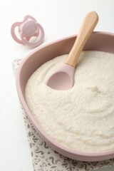 Delicious baby food in bowl with spoon and pacifier on white background, closeup