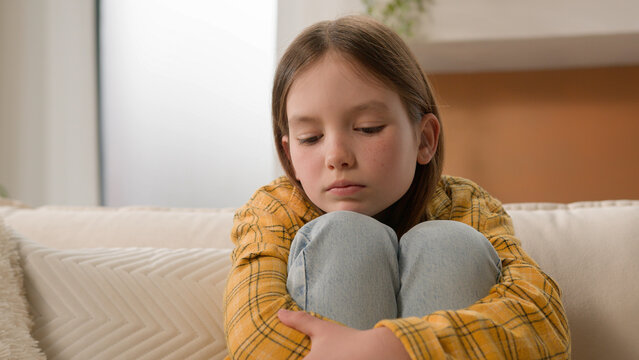 Stressed unhappy sad pensive Caucasian kid little girl feeling frustrated depressed lonely hugging knees alone child bored anxious punished daughter thinking family abuse problems home couch apartment