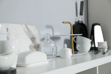 Different kitchenware on white shelf near grey wall indoors, closeup