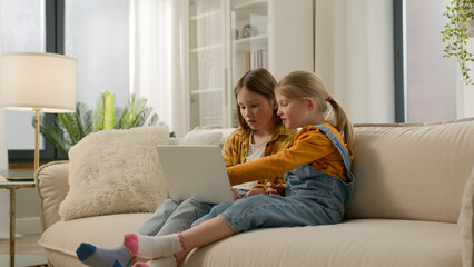 Carefree Caucasian kids daughters family girls watching movie funny cartoon on laptop computer. Happy children little sisters talk friendly conversation playing pc games chatting online couch at home