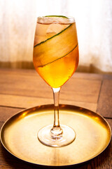 Cocktail in a tall glass in front of a curtained window standing on a brass platter