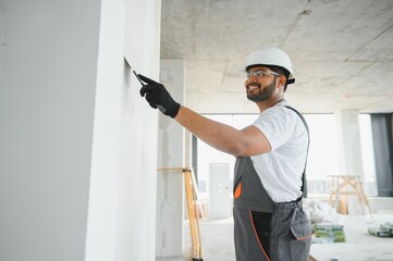 Professional indian worker plastering wall with putty knife indoors.