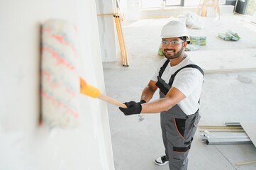 An Indian apartment repair worker paints a white wall with a roller