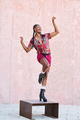 Gay man in red shirt and shorts dances on a stool