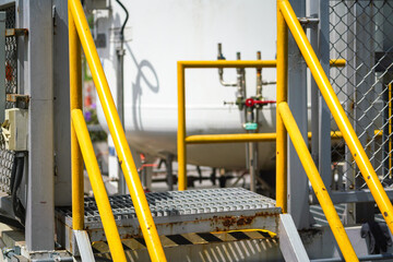 Refinery plant and oil storage metal walkway-stair platform with yellow handrail or banister rail part. Industrial workplace, close-up and selective focus.