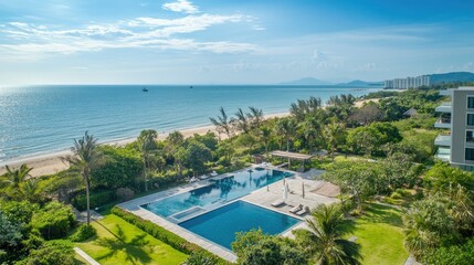 Fototapeta premium Aerial view of a serviced condominium for rent in Hua Hin, featuring a swimming pool, tropical greenery, and stunning views of the sea and beach under a sunny sky