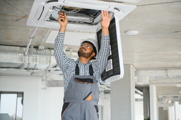 Indian male worker inspecting the air conditioner mounted on the ceiling