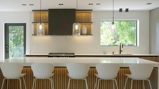 Set of white bar stools standing next to table in row in kitchen with overhead light and glass door leading outside. Apartment with combination of white and wood in interior