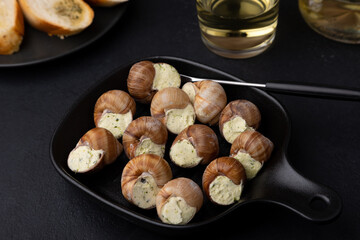 Escargot bourguignon with butter and garlic. Traditional French dish made from snails, served with baguette and white wine. Selective focus, close-up, black background.