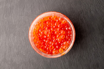 Red caviar in a glass jar on a slate stone, macro, top view.