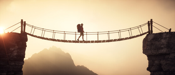 Hiker walking on a suspension bridge between mountains.