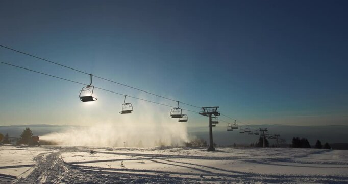 Sunset silhouette of a chairlift on a snowy mountain top in Kopaonik, casting shadows against the serene winter landscape and highlighting the peaceful beauty of a ski resort at dusk.