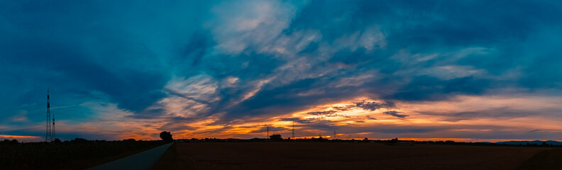 Sunset with a dramatic sky and overland high voltage lines near Tabertshausen, Aholming, Deggendorf, Bavaria, Germany