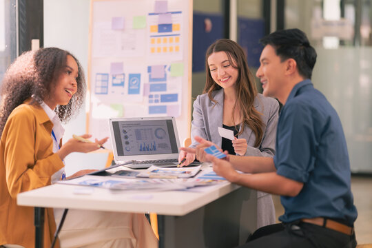 A team of UI UX web designers are working together to develop a mobile responsive website while discussing a project at a modern conference table. Brainstorming