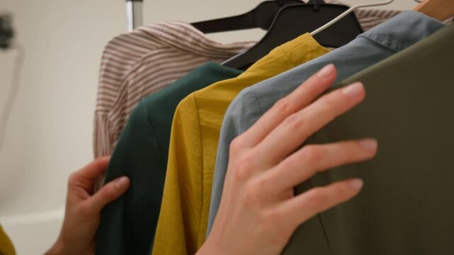 Trendy Caucasian woman female choosing touching clothes deciding outfit fashion stylish model blog getting ready for work hands picking up girl blogger grab green shirt on hangers wardrobe in studio