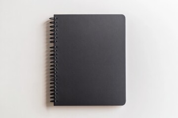 Mockup of an empty black spiral notebook with sleek, matte black covers, neatly centered on a clean white background, perfect for design presentations or branding visuals, copy space for text