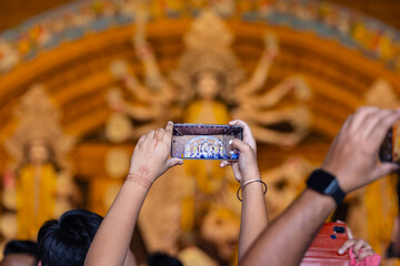 Shubho mahalaya, Hand holding mobile phone and taking photos of Goddess Durga idol at a pandal...