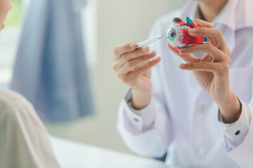 Ophthalmologist using anatomical model of eye to explain to patient with vision problem in...