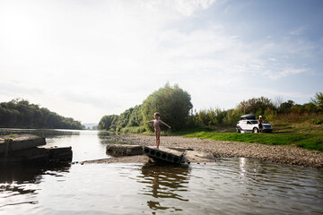 Fototapeta premium Child balancing on pier by riverside with parked car nearby