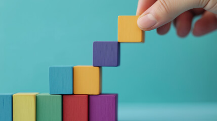 Obraz premium Colorful wooden blocks in a hand forming a staircase against a blue background