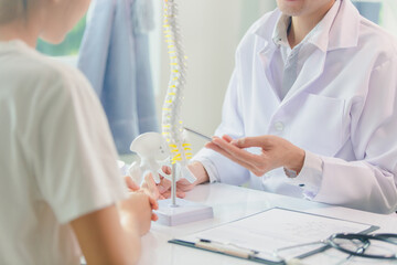 An orthopedic doctor shows a spinal model to a patient in a human spinal hospital. Diseases and...