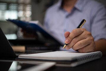 Business professional taking notes in a notebook while reviewing documents at a desk planning organization and business strategy development. Represents business analysis.