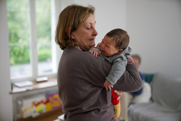 Elderly woman comforting a crying newborn baby, emphasizing a nurturing and loving environment. The scene captures a tender moment of care and affection.