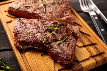 Grilled beef steak, well done with seasons and green on a black wooden background close up