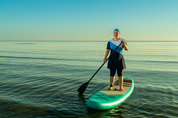 Woman in a sports suit for swimming on a paddleboard with a paddle in the sea against the background