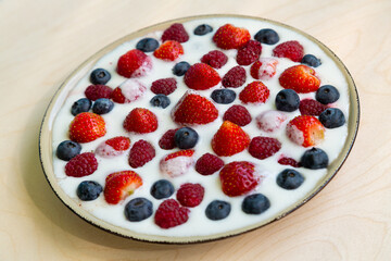 In a plate with whipped cream, strawberries, raspberries and blueberries on the table