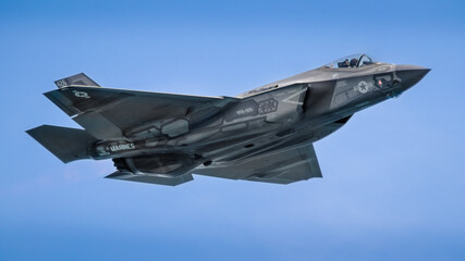 Dynamic photo of a F-35 military jet in flight against a clear blue sky, showcasing the advanced...