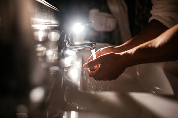 closeup of a young caucasian man washing his hands in the sink in bathroom