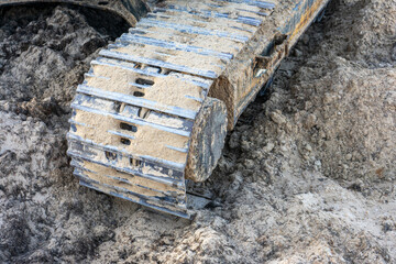 Close-up of excavator caterpillars on rough terrain, showcasing detailed treads and dirt accumulation. Ideal for construction and machinery themes.
