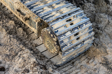 Close-up of excavator caterpillars on rough terrain, showcasing detailed treads and dirt accumulation. Ideal for construction and machinery themes.