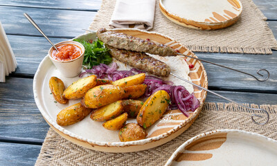 Georgian lula kebab with baked potatoes, sauce and greens. Grilled souvlaki, minced meat kebap, lamb on skewers