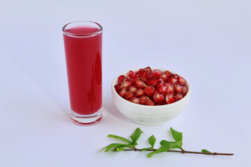 Punica granatum in a cup and red-purple juice in a glass together with leaves on a white background.