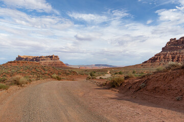 A dirt road leading through Valley of the Gods in Utah with red rocks and open desert.