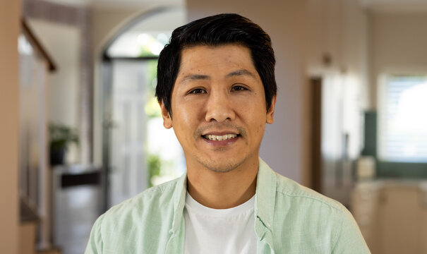 Smiling asian man in casual shirt standing in modern home interior