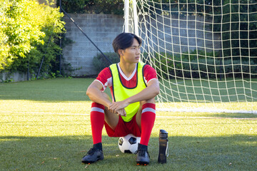 Resting on soccer field, athlete in uniform with soccer ball and water bottle