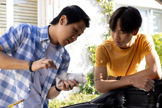 Checking car oil level, father teaching son about car maintenance outdoors